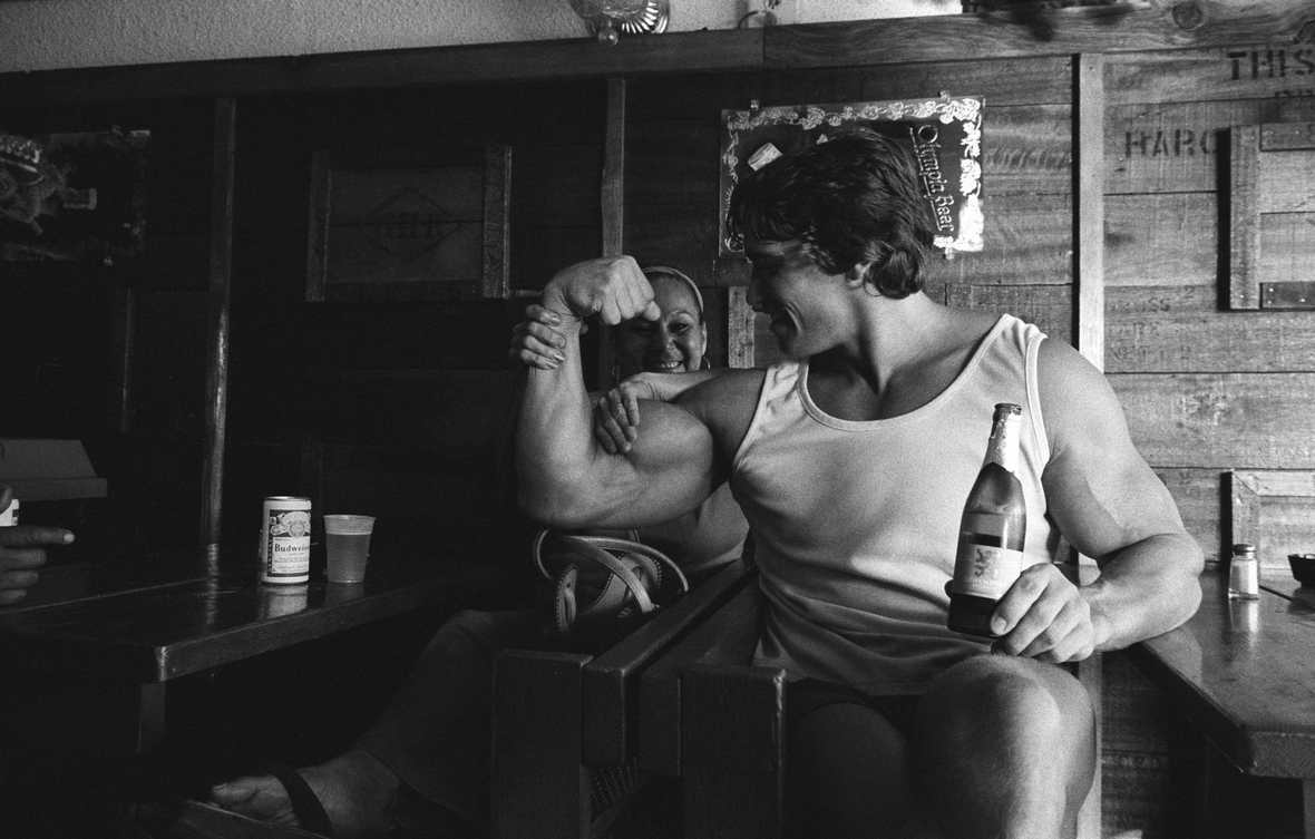 На фото Арнольд Шварцнеггер в пивном баре с бутылкой пива.